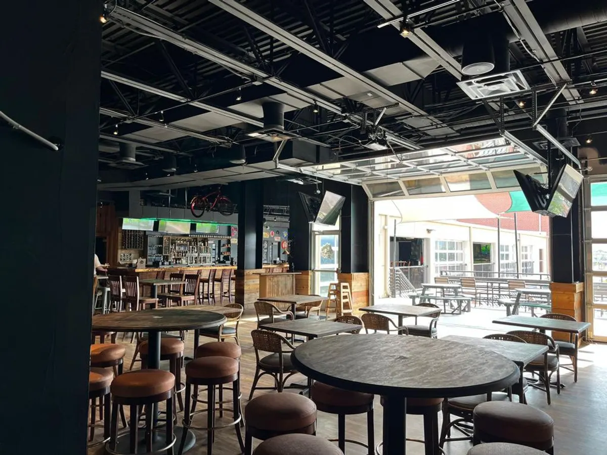 The same room in daylight, quiet and half empty, with long wooden tables and high stools along the windows.